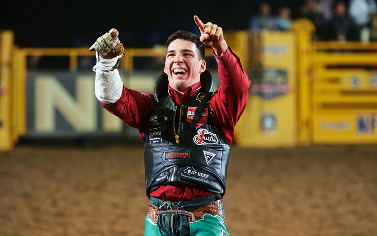 Jess Pope smiling and pointing up with both hands wearing his bareback riding equipment.